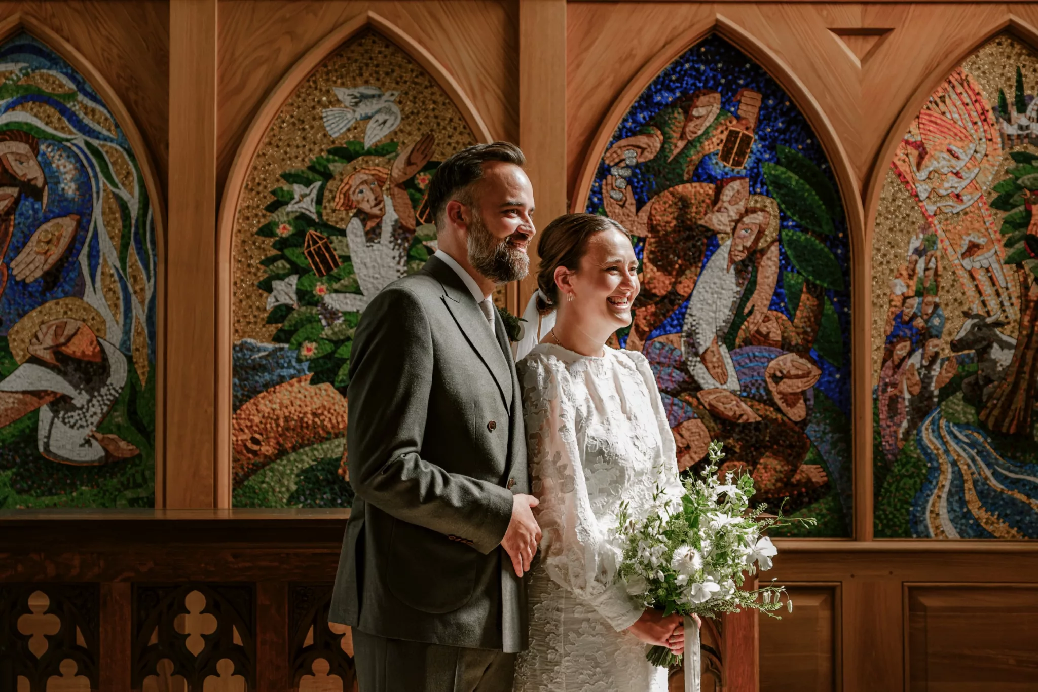 Bride and groom in dramatic church lighting, standing in front of a beautifully ornate high altar at their wedding in the Cotswolds.