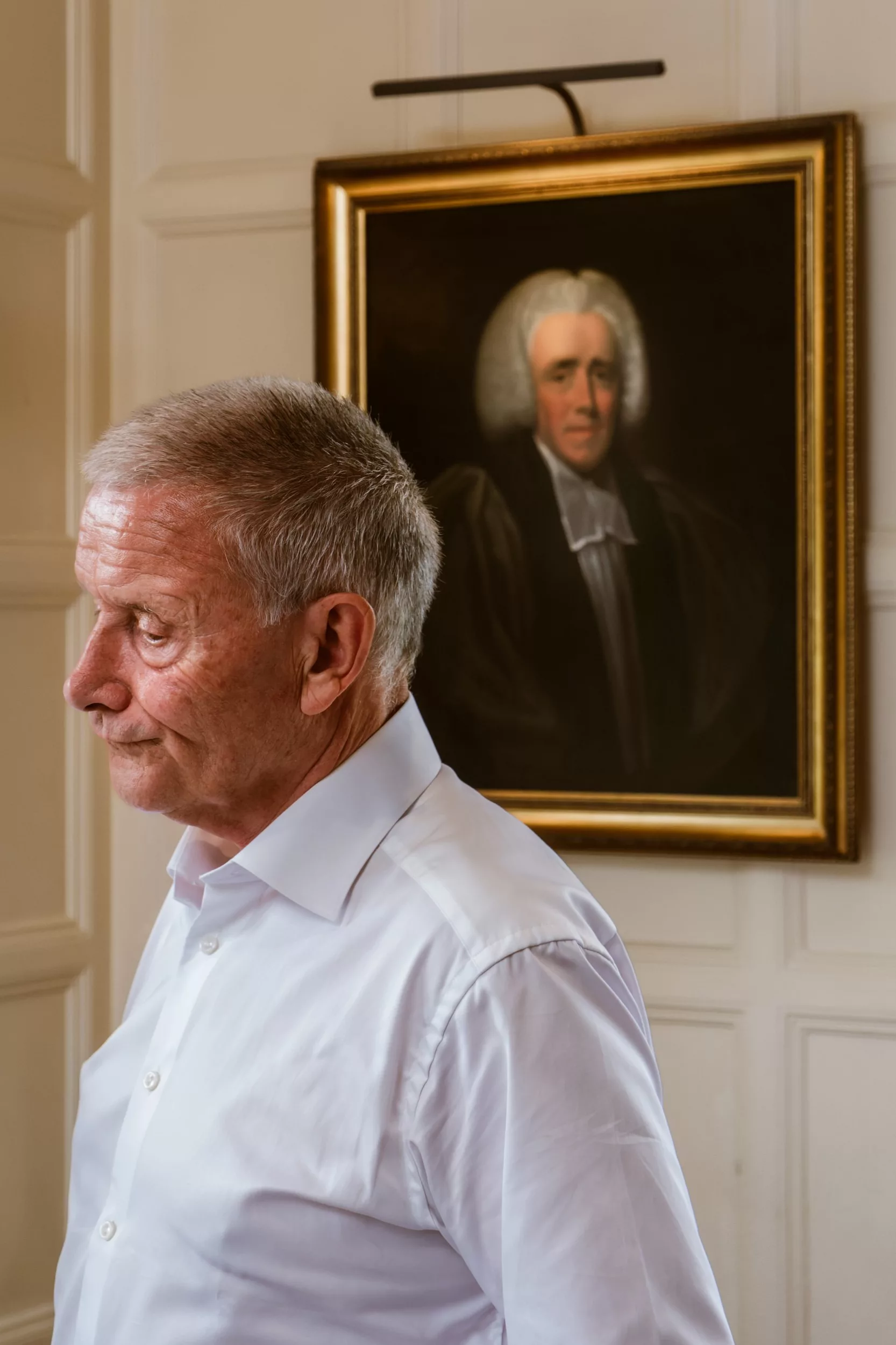 A funny moment showing a groom with a dismayed expression on his face, mirroring the worried expression of a man in a painting behind him on the wall.