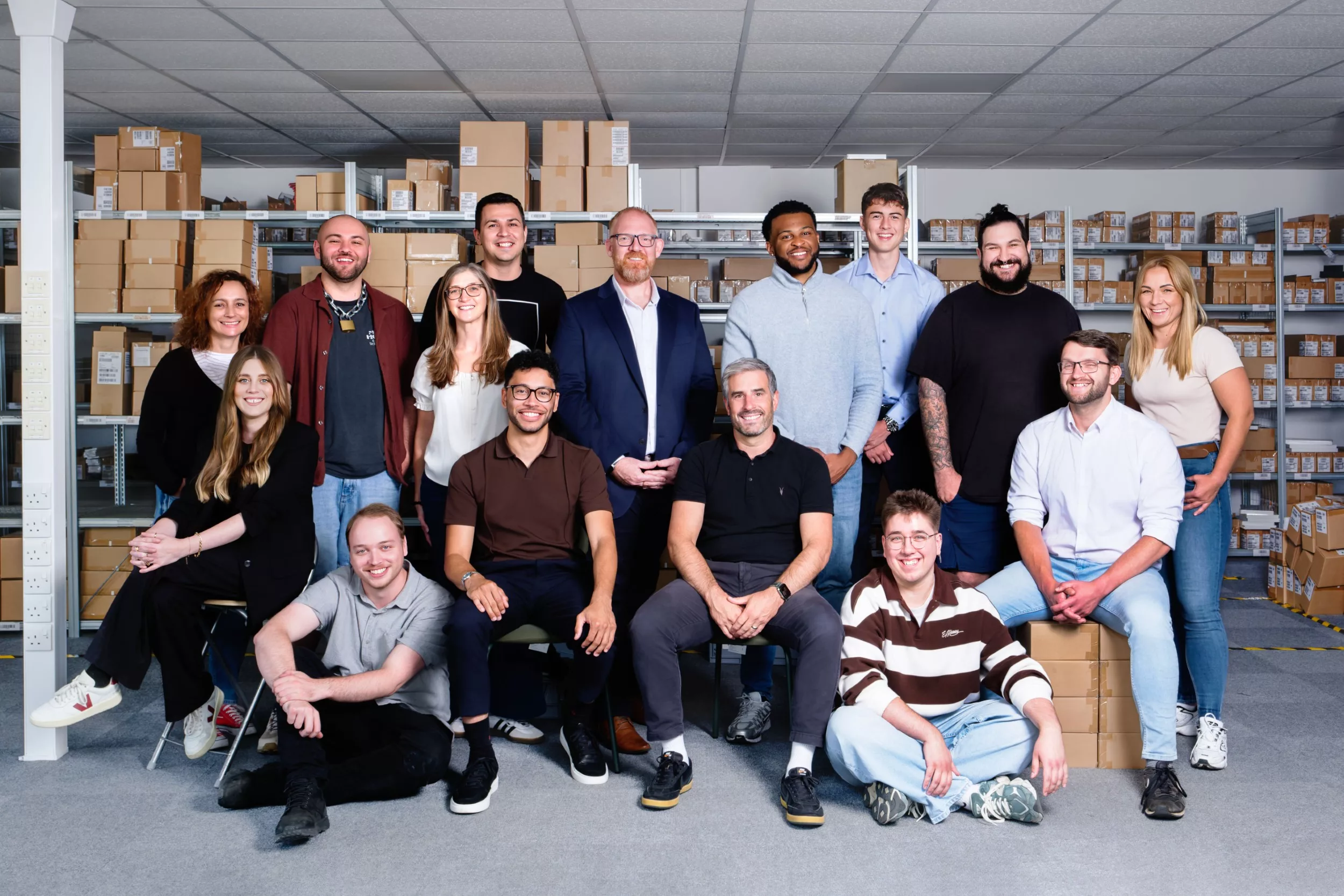 A big group of employees posed inside a warehouse for a team portrait, lit and posed carefully for a relaxed but professional effect.